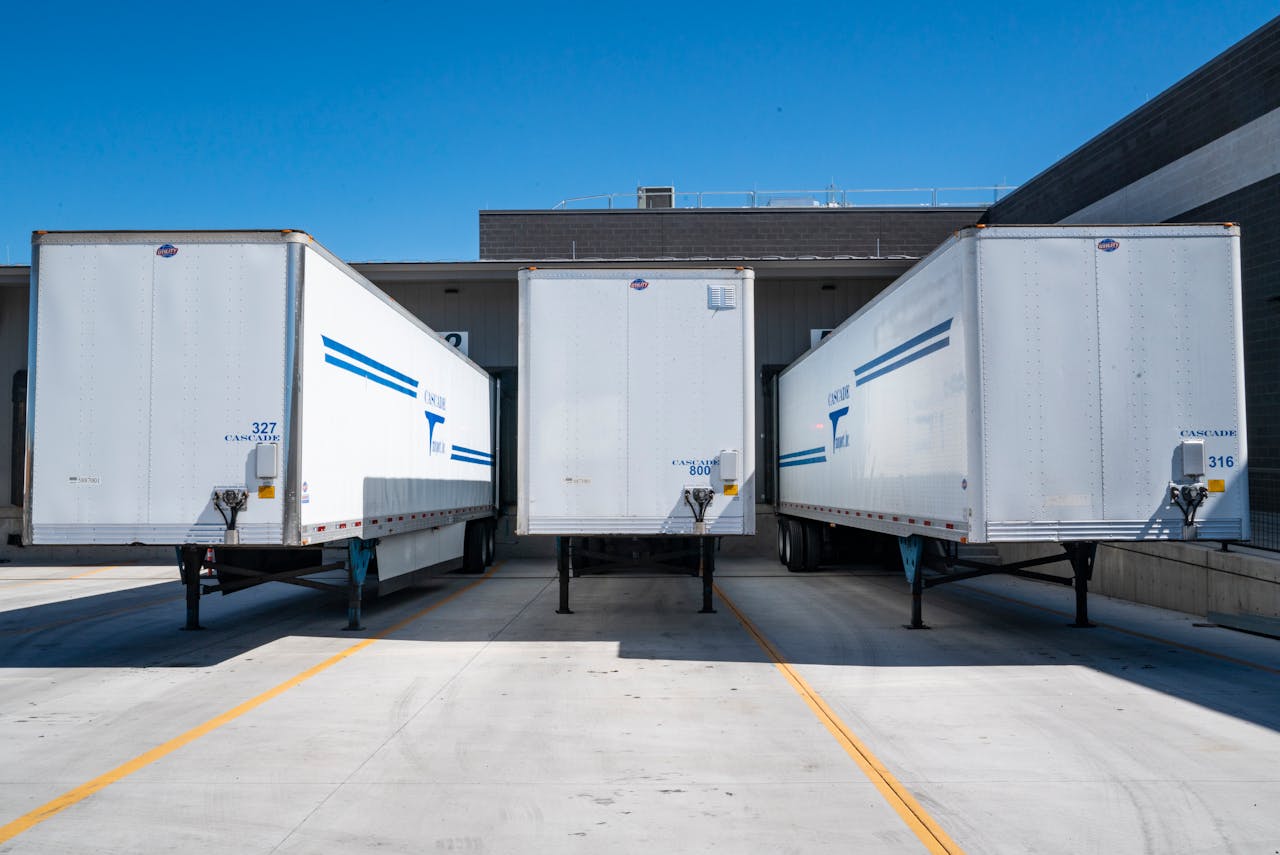 Home Three white cargo trailers parked at an industrial shipping dock under clear blue skies.